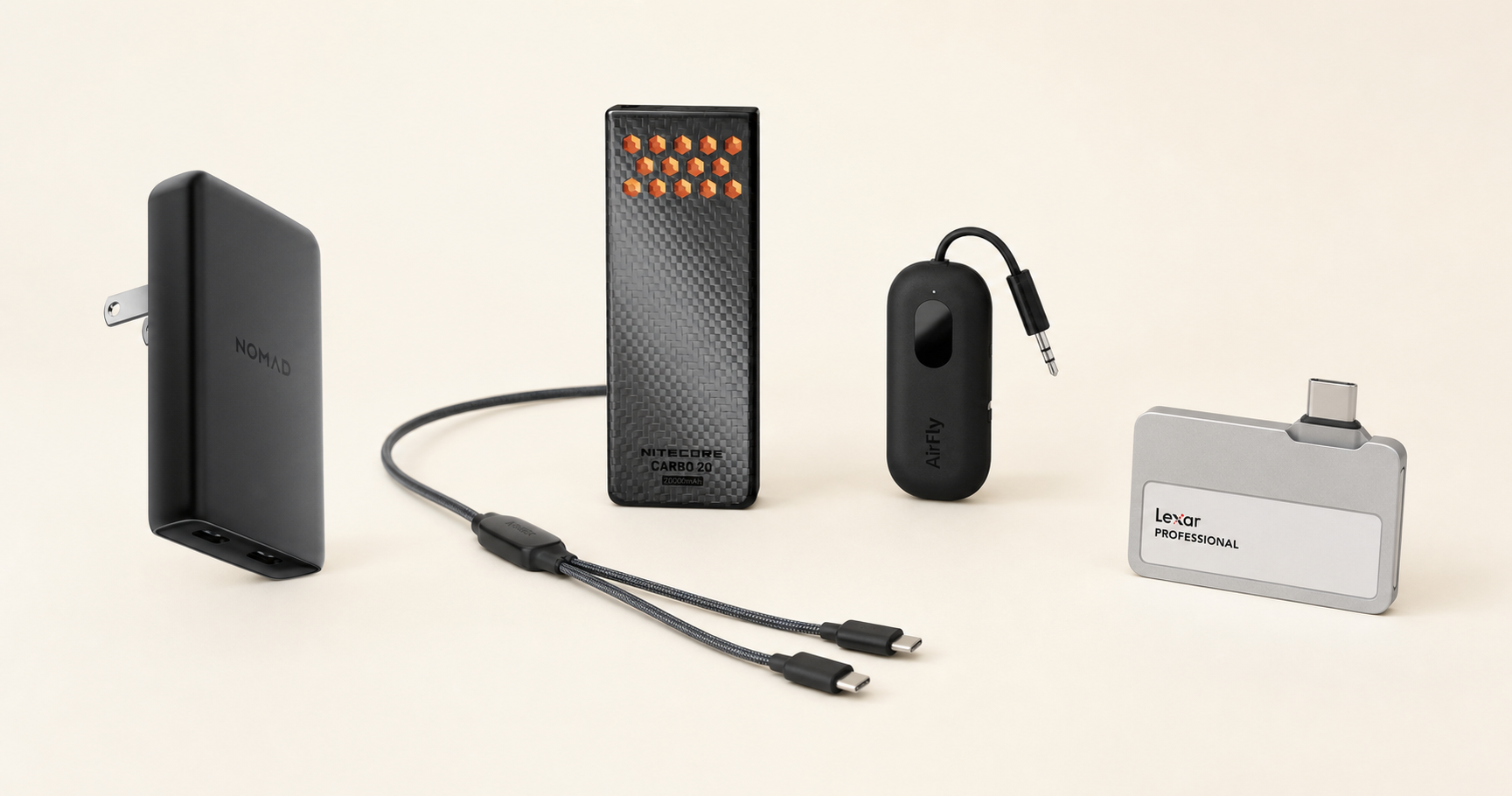 Nomad charger, Anker split cable, Nitecore power bank, AirFly, and Lexar SSD arranged as a compact carry-on tech kit